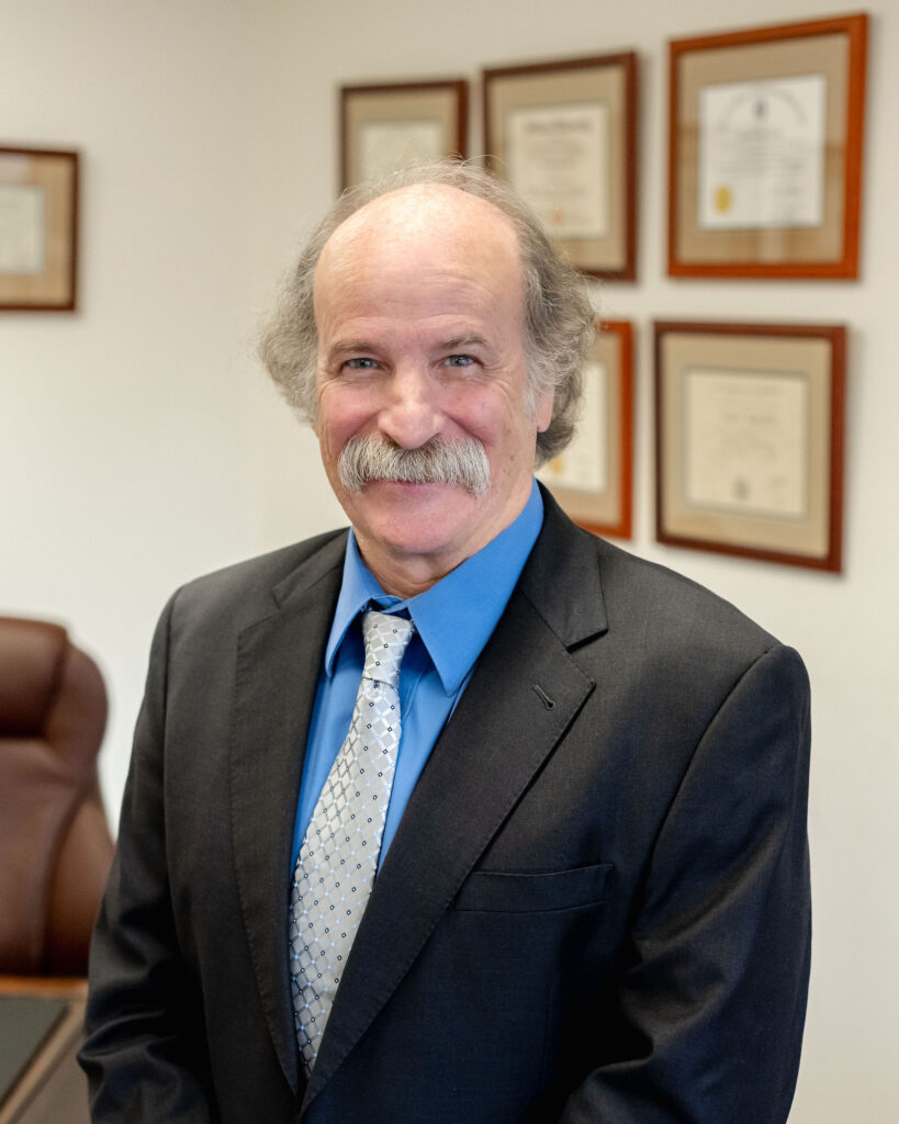 Professional portrait of Dr. Roger Light, PhD, ABPP, ABCN, standing in his office at The Light Center, with framed credentials in the background