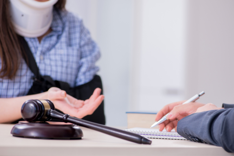 Woman with neck brace and arm sling discussing a personal injury claim with a legal professional, gavel on table